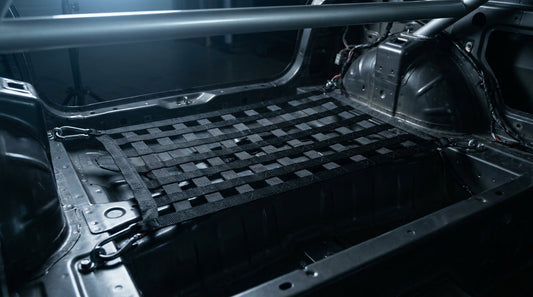 A precisely fitted custom cargo net stretched taut across the stripped boot interior of a track-prepared car, highlighting clean attachment points and tight weave craftsmanship.